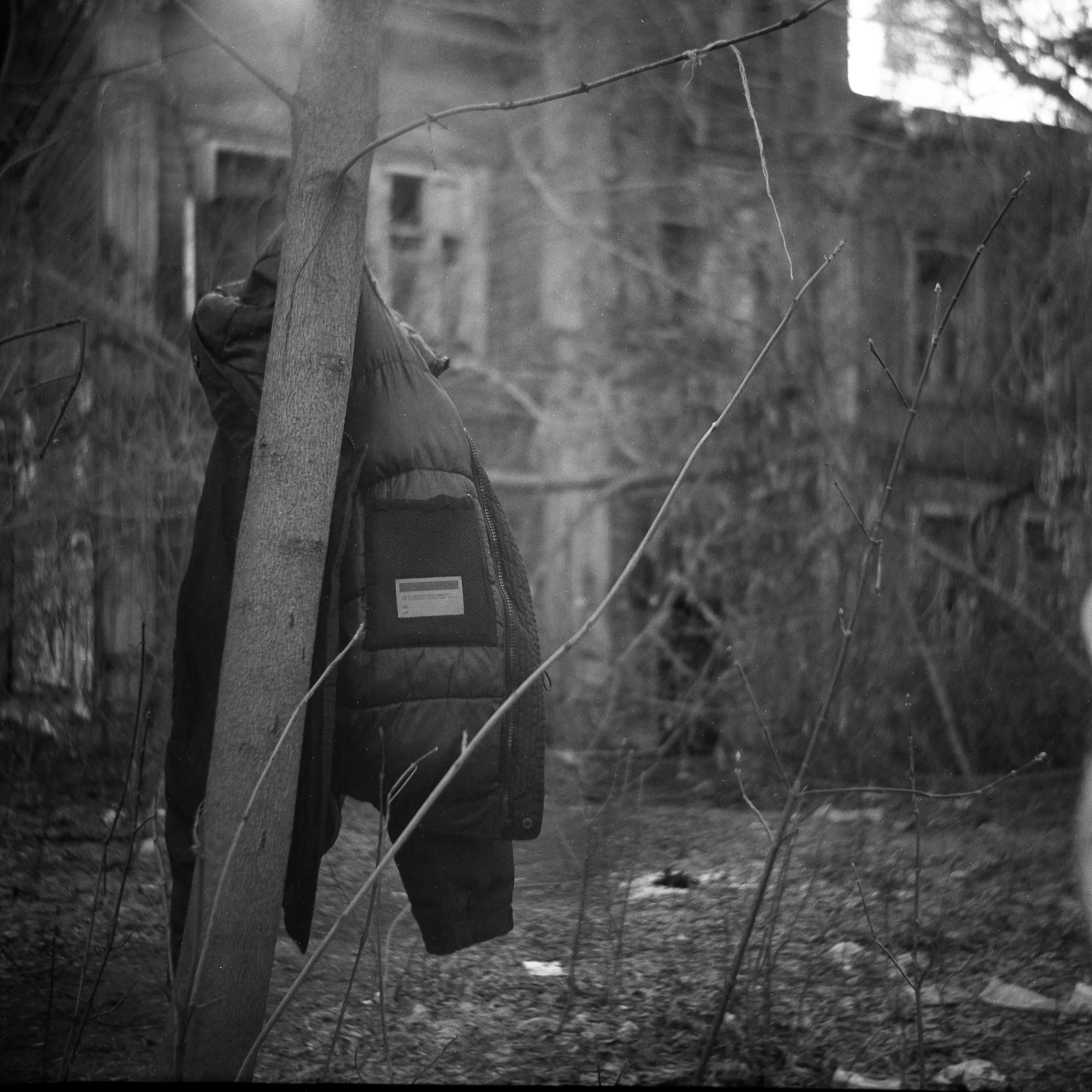 photo of a jacket on a tree with an old house at the background taken with a soviet camera